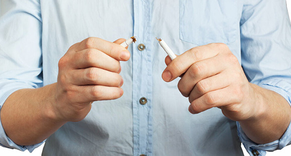 a person snapping a cigarette in half, with the tobacco spilling out