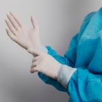 Healthcare professional wearing protective medical clothing and latex gloves while preparing for a clinical procedure.