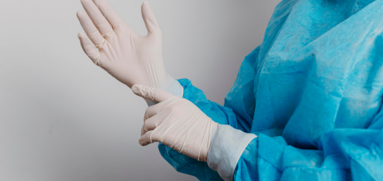 Healthcare professional wearing protective medical clothing and latex gloves while preparing for a clinical procedure.