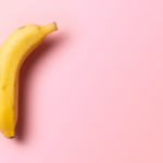 Single yellow banana on a pink background, positioned to highlight its curved shape with ample empty space around it.