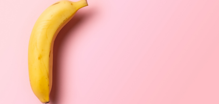 Single yellow banana on a pink background, positioned to highlight its curved shape with ample empty space around it.