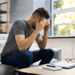 Man sitting on a sofa with his head in his hands, illustrating the emotional impact of leaving Peyronie’s disease untreated.