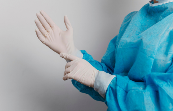 Healthcare professional wearing protective medical clothing and latex gloves while preparing for a clinical procedure.