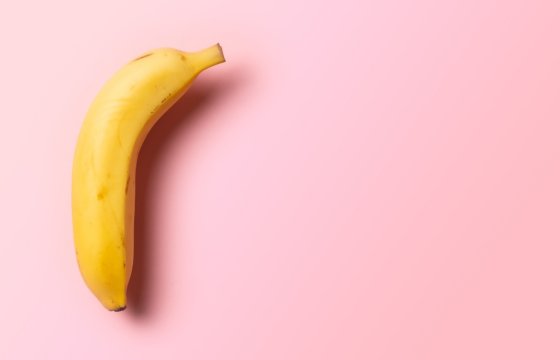 Single yellow banana on a pink background, positioned to highlight its curved shape with ample empty space around it.